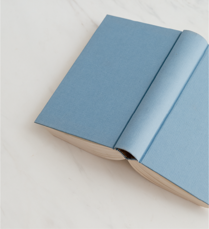 Asset 16@3x ScopeSchool An open book with a plain light blue cover lies on a white surface, partially closed with the top right corner folded over.