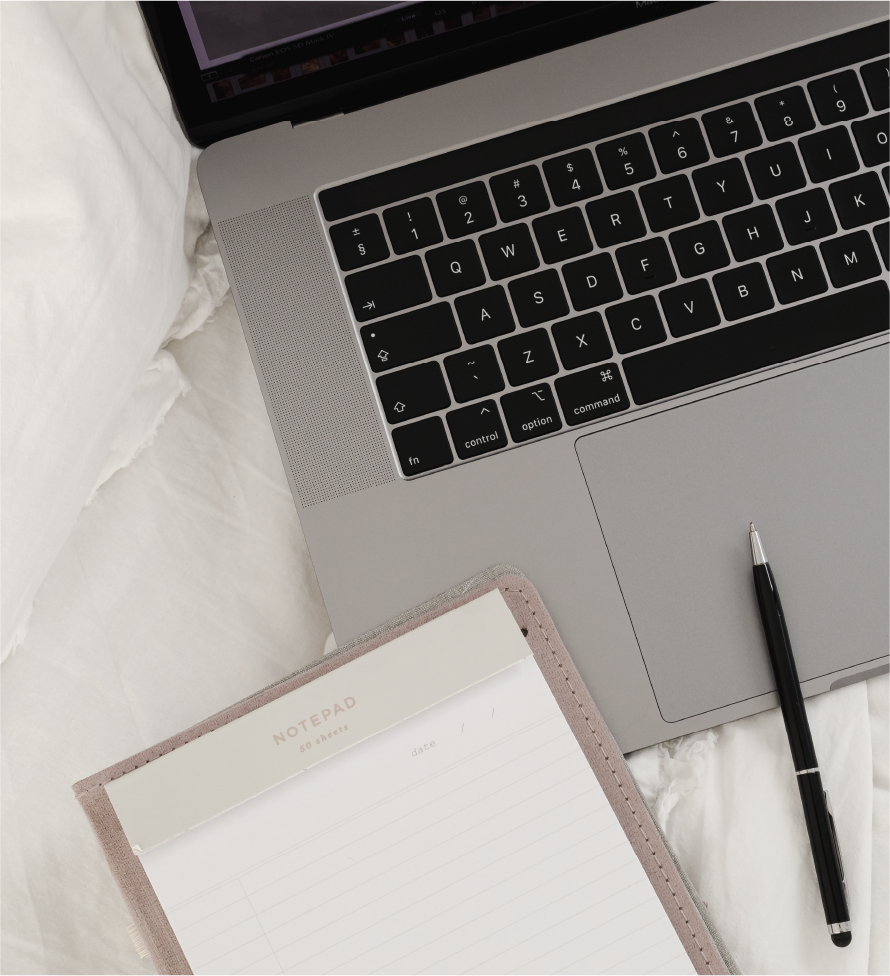 Asset 18@3x ScopeSchool A notepad and pen are placed next to an open laptop on a white bed.